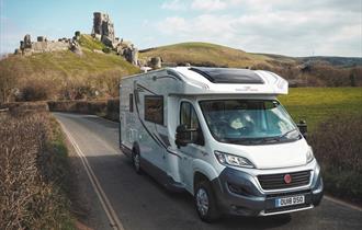 Campervan driving along road with corfe castle in the background