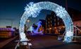 Archway of Christmas lights with a Blue lit up anchor in the background