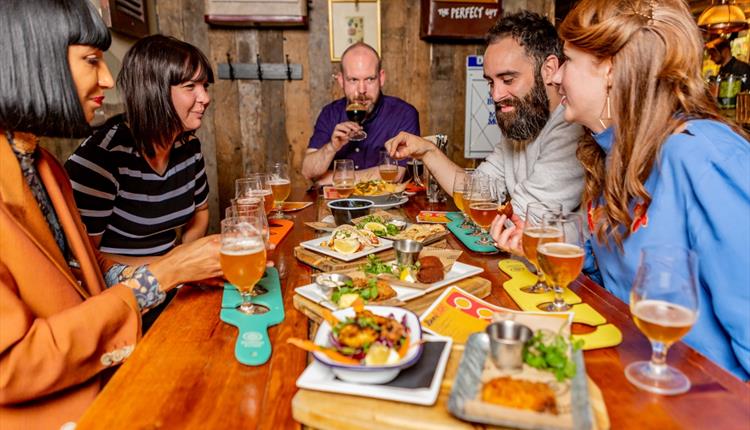 Five people around a table enjoying a selection of food and beer.