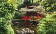 Red Japanese house and pond surrounded by trees and flowers.