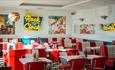 Red and white tables inside the diner with 50s Americana decoration on the walls.
