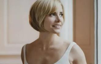 Dame Darcey Bussell DBE gazing away from the camera, smiling with a white leotard on with a short fringe bob haircut.