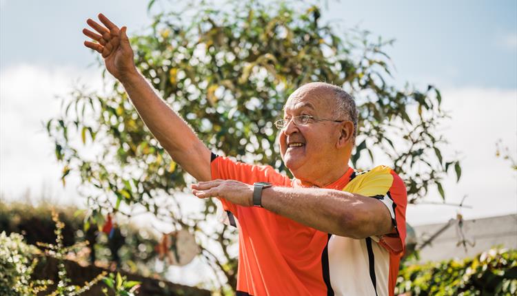 Man with bright colour block shirt smiling and holding hands in the air