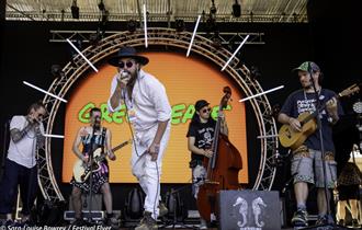 5 piece band with singer dressed in white in the foreground and a large metal sphere surrounding them