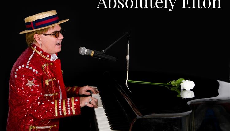 Man with red glitter suit and hat sitting by a piano