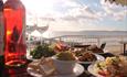 Selection of food and bottle of wine on a table overlooking the sunset views of the beach