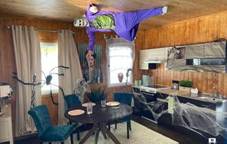 Upside down house decorated spookily with cobwebs with a person dressed up as a joker.