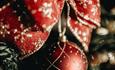 A close up image of a red Christmas bauble and red bow, placed on a green Christmas tree