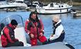 Three people sat on the front of a powerboat talking with lifejackets on