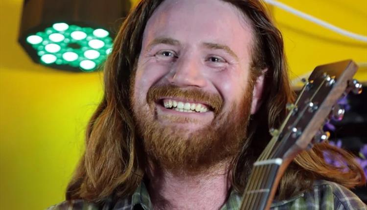 Close up of long haired male holding his guitar wearing a check shirt with a yellow background