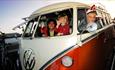 Father and children smiling at the camera in their red VW campervan