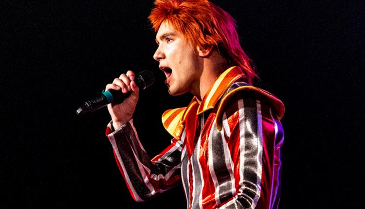 Image of man in a stripe costume, singing in a microphone