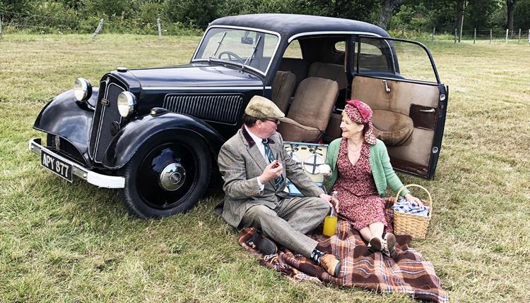 Couple dressed in vintage clothes whilst enjoying a picnic next to their old car