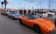 Visitors looking at the orange sports car and other cars lined up alongside Poole quay