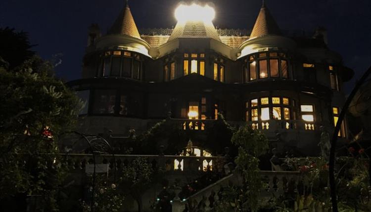 A spooky Russel-Cotes house with a dark sky and brightly lit up windows and roof.