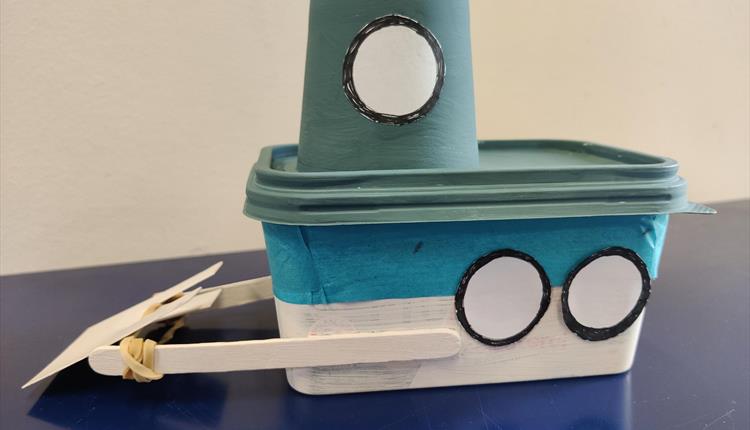 White and blue paddle boat made from a painted butter tub with a cabin and propeller