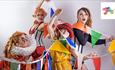 four actors dressed up as clowns from the circus tangled up in colourful bunting