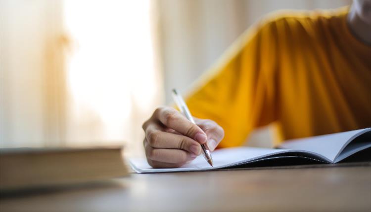 Young person's hand holding a pen and writing in a notebook.