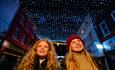 Two girls walking down the highstreet with Christmas lights overhead