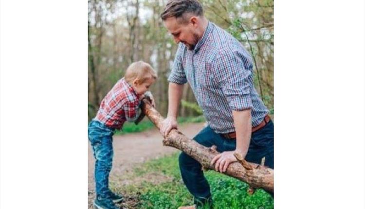 A dad and his young son outdoors holding a stick