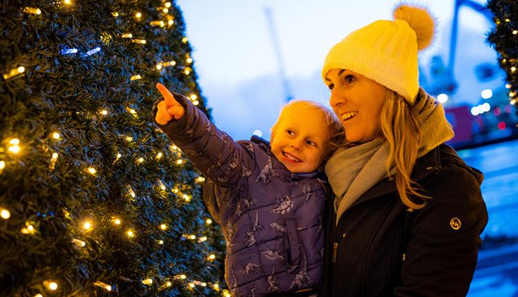 Woman dressed up for winter whilsy holding her child who is pointing at the Christmas lights
