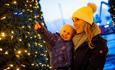 Woman dressed up for winter whilsy holding her child who is pointing at the Christmas lights