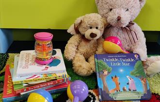 Two teddy bears reading a board book with some musical rattles