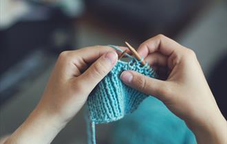 Image shows someone knitting with blue wool.