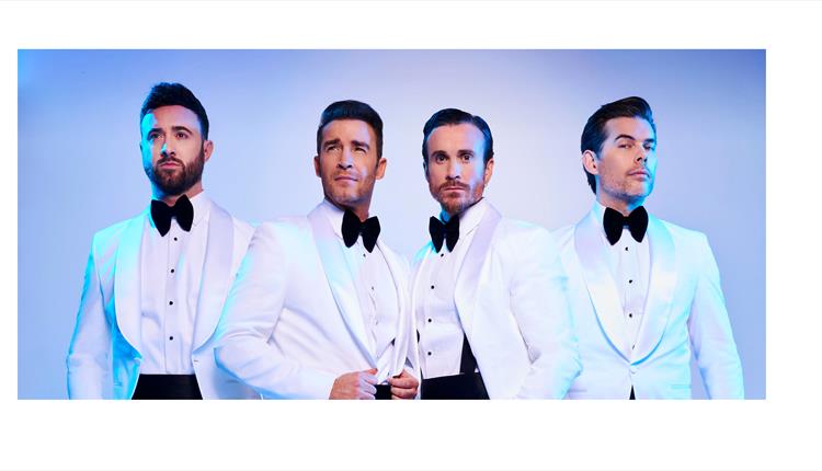 The Overtones wearing smart white tuxedo suits and black bow ties posing for camera with a light lilac background