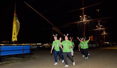 Participants in the Shining Stars Walk walking past HMS Warrior, with Spinnaker Tower in the background