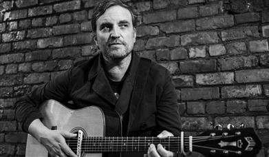 Black and white photograph of James Walsh with an acoustic guitar