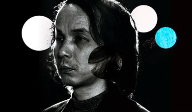 Black and white photograph of composer Tōru Takemitsu with white and blue balls in the background