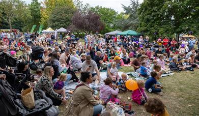 Lots of family groups sat on grass with gazebos in the background.