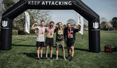 Four men with medals stood in front of an inflatable arch saying Keep Attacking.