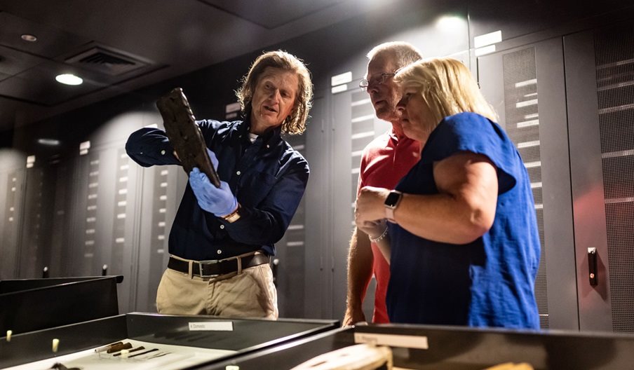 A member of the Mary Rose Museum team showing an artefact to a man and woman.