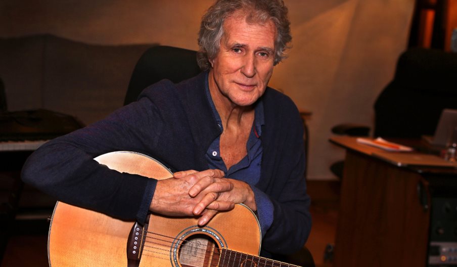 Photograph of John Illsley holding an acoustic guitar