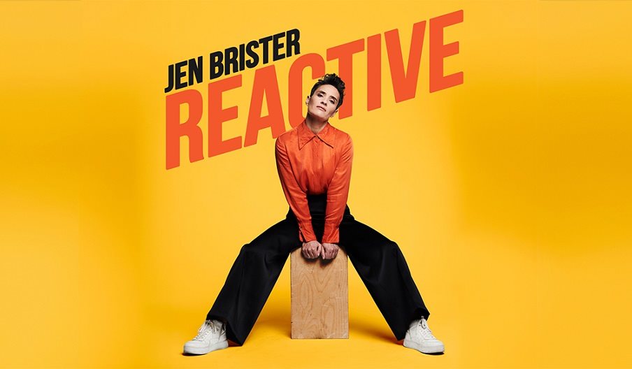 Comedian Jen Brister sat on a wooden box.