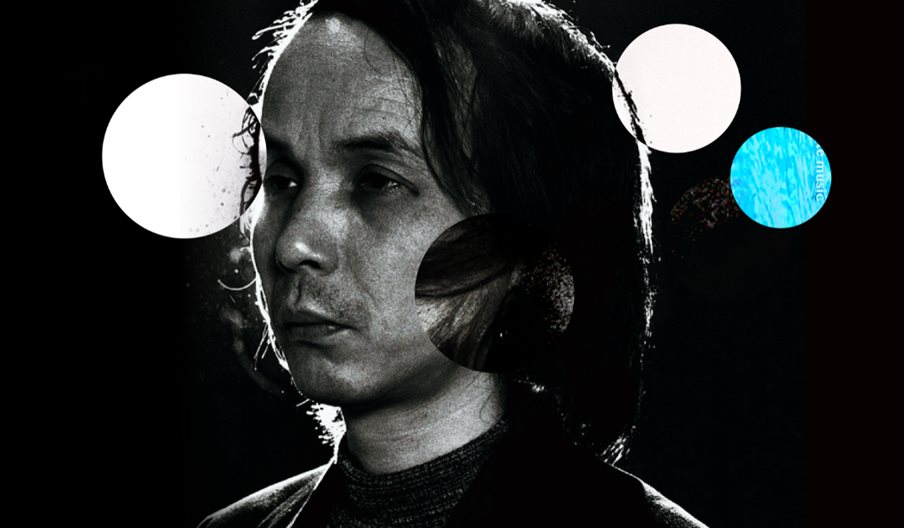 Black and white photograph of composer Tōru Takemitsu with white and blue balls in the background