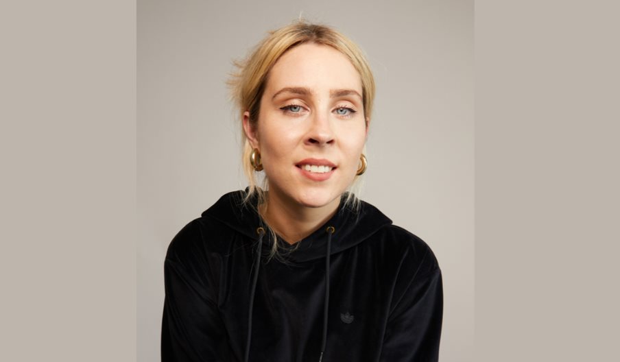 Poster image for Stevie Martin: Clout, showing the comedian in a black hoodie and stood against a brown background