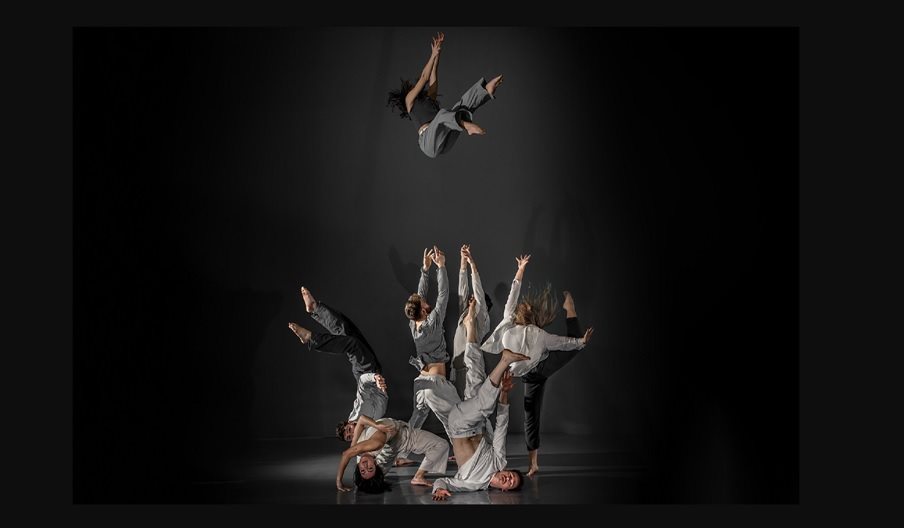 A group of dancers dressed in grey clothes one of the dancers has been thrown up.
