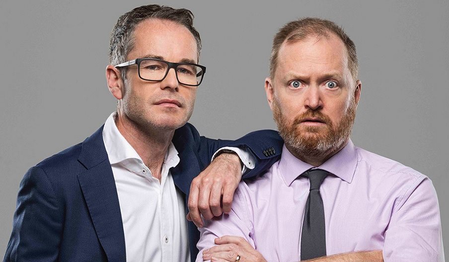Two white men, one wearing glasses with a shirt and jacket. The other has a beard with a shirt and tie.
