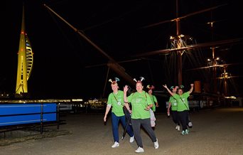 Participants in the Shining Stars Walk walking past HMS Warrior, with Spinnaker Tower in the background