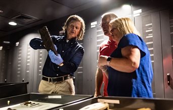 A member of the Mary Rose Museum team showing an artefact to a man and woman.