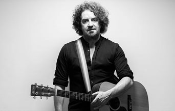 Black and white photograph of Ian Prowse holding an acoustic guitar.