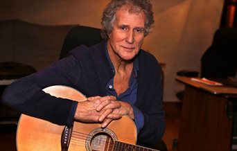 Photograph of John Illsley holding an acoustic guitar