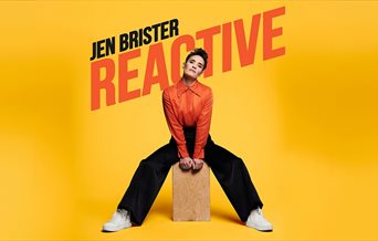 Comedian Jen Brister sat on a wooden box.