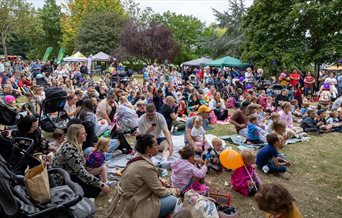 Lots of family groups sat on grass with gazebos in the background.