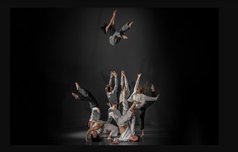 A group of dancers dressed in grey clothes one of the dancers has been thrown up.