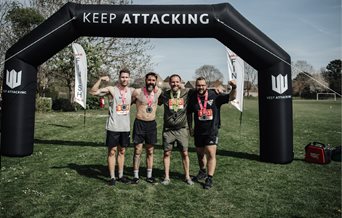 Four men with medals stood in front of an inflatable arch saying Keep Attacking.