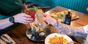 Cheers! Two people clink glasses over plates of freshly prepared food.